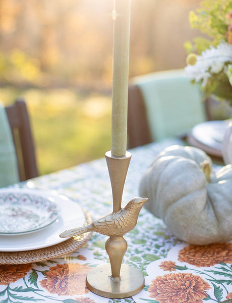 Decorative candlestick with bird design on a table setting with pumpkins and floral tablecloth.